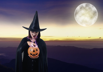 woman in Black Scary witch halloween costume holding pumpkin witch's cauldron smoke coming out with moonlight. landscape mountain and sea of mist