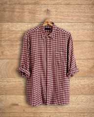 Plaid shirt long sleeve hanging on wooden background.