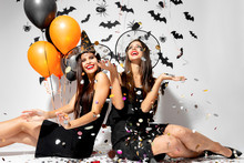 Two Brunette Women In Witches Hats Smile, Have Fun With Confetti And Hold Black And Orange Balloons. Halloween