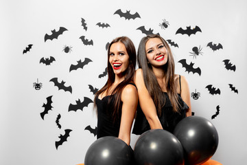 Gorgeous brunette woman in black dress holds black and orange balloons on a white background with black bats and spiders. Halloween