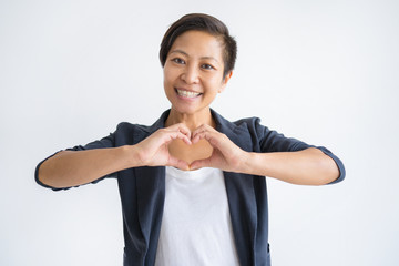 Wall Mural - Smiling Asian woman making heart gesture with her hands. Young lady looking at camera. Love concept. Isolated front view on white background.