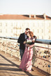© olegparylyak - Stylish loving wedding couple, groom, bride with pink dress kissing and hugging on a bridge at sunset