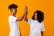 Excited emotional young cute african couple posing isolated over yellow background give a high five to each other.