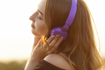 Wall Mural - teenager girl in headphones listening to music on nature, young woman is relaxing in the summer field