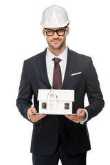 Wall Mural - confident young male architect in hard hat showing miniature house isolated on white