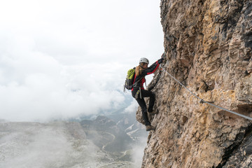 young attractive female university student on a vertical and exposed rock face climbs a Via Ferrata in Alta Badia in the South Tyrol