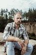 © Viacheslav Yakobchuk - Blonde-haired model. Handsome blonde-haired model wearing jeans and squared shirt posing for photo while sitting on rock near canyon