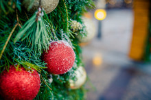 Christmas Family Atmosphere.Red,golden Christmas Ornament Hanging On A Frost Covered Pine Tree Outdoors With Copy Space.Christmas Decoration With Lots Of Lights.blurred Lights And Outdoor Decorations