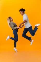 Poster - Young loving couple jumping isolated over yellow background.