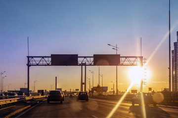 Wall Mural - City highway road with busy traffic at sunset evening time. Beautiful metropolis cityscape with dramatic multicolored sky on background. Dusk lens flare.