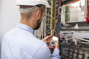 Young adult electrician builder engineer inspecting electric equipment in distribution fuse box. Electrical engineer worker in control panel. Maintenance electro box with multimeter