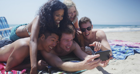 Wall Mural - Young adult group of multi ethnic friends lying on sand taking selfie