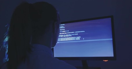 portrait of young woman hacker programmer working at a computer at night in data center. Back view.