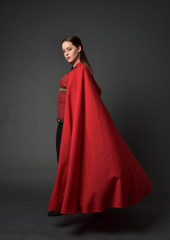 Canvas Print - full length portrait of brunette girl wearing red medieval costume and cloak. standing pose  in side profile,   on grey studio background.