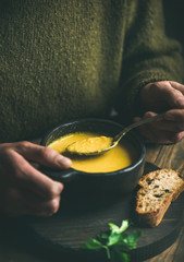 Wall Mural - Man in dark green winter sweater eating sweet corn and shrimp chowder soup from black bowl with toasted bread, close-up. Autumn or winter warming food