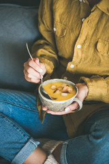 Female in denim jeans and mustard shirt sitting keeping mug of Fall warming pumpkin cream soup with croutons top view. Autumn vegetarian, vegan, healthy comfort food eating concept