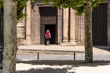 Spain, La Rioja, Navarrete: Pilgrim with red backpack enters pilgrim Church of Santa Maria de la Asuncion in the city center of the Spanish town - concept Way of St. James religion pilgrimage church