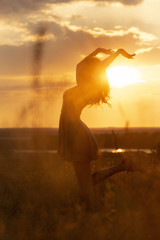 Wall Mural - silhouette of a beautiful dreamy girl at sunset in a field, a young woman idance with happiness on nature