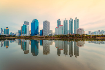 Wall Mural - sunrise on morning city building skyline of skyscraper and green park with water reflection in downtown the cityscape landmark in Bangkok Thailand for business city and travel center.