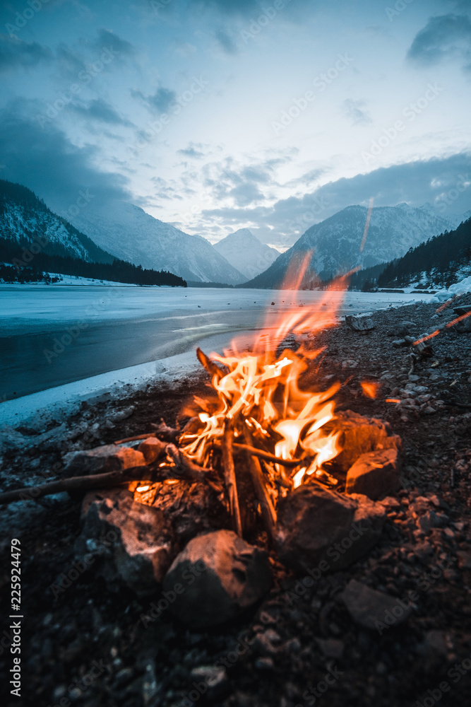  Winter campfire in the top of a frozen lake at night, a magnificent view of the mountains at sunset. Traveler's Life - obrazy, fototapety, plakaty 