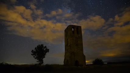 Wall Mural - the milky way moving across the night sky and an ancient castle tower in a partly cloudy summer nigh