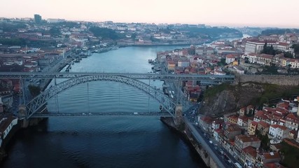 Wall Mural - Flying over Douro river and Dom Luis I iron bridge early morning in Porto, Portugal. Aerial view of the old city center.