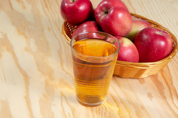 Wall Mural - Glass of apple juice in front of a basket full of red ripe apples