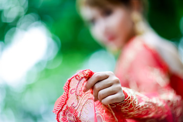 Close up bride’s hand wears thai traditional wedding dress, red lace fabric and ancient gold bracelet. No face. Thai traditonal wedding clothes.