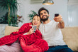 © Mediteraneo - Beautiful young couple watching TV in living room.