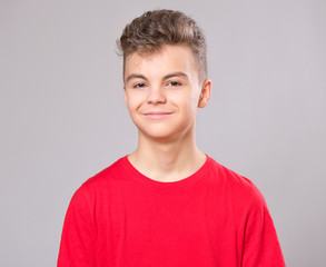 Wall Mural - Close up emotional portrait of caucasian teen boy. Handsome smiling guy. Funny cut teenager on gray background. Child looking at camera.