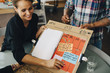 © Maskot - smiling businesswoman showing strategy on placard to colleague in office