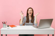 © ViDi Studio - Laughing woman in casual clothes holding pencil spreading hands sit, work at white desk with contemporary pc laptop isolated on pastel pink background. Achievement business career concept. Copy space.