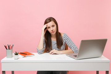 Wall Mural - Concerned upset tired woman leaning on hand sit, work at white desk with contemporary pc laptop isolated on pastel pink background. Achievement business career concept. Copy space for advertisement.