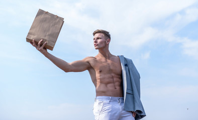 Wall Mural - Guy attractive macho carry shopping bag made out of brown paper. Eco package. Sales season. Shop assistant concept. Man muscular athlete hold shopping bag sky background. Hot sales and discount