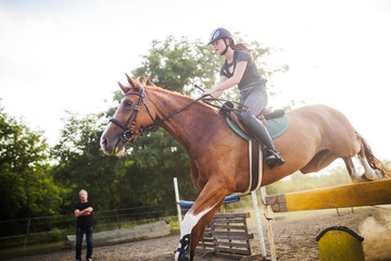 Young female jockey on horse leaping over hurdle