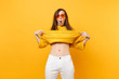 Portrait of shocked funny young woman in heart orange glasses taking off fur sweater, showing belly isolated on bright yellow background. People sincere emotions, lifestyle concept. Advertising area.