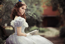 Beautiful Girl In Historical Dress, Gloves, With A Book In Her Hands Sitting On The Bench