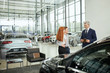 © alfa27 - Sales agent at the table desk telling about car features to cheerful couple of customers at car dealership office