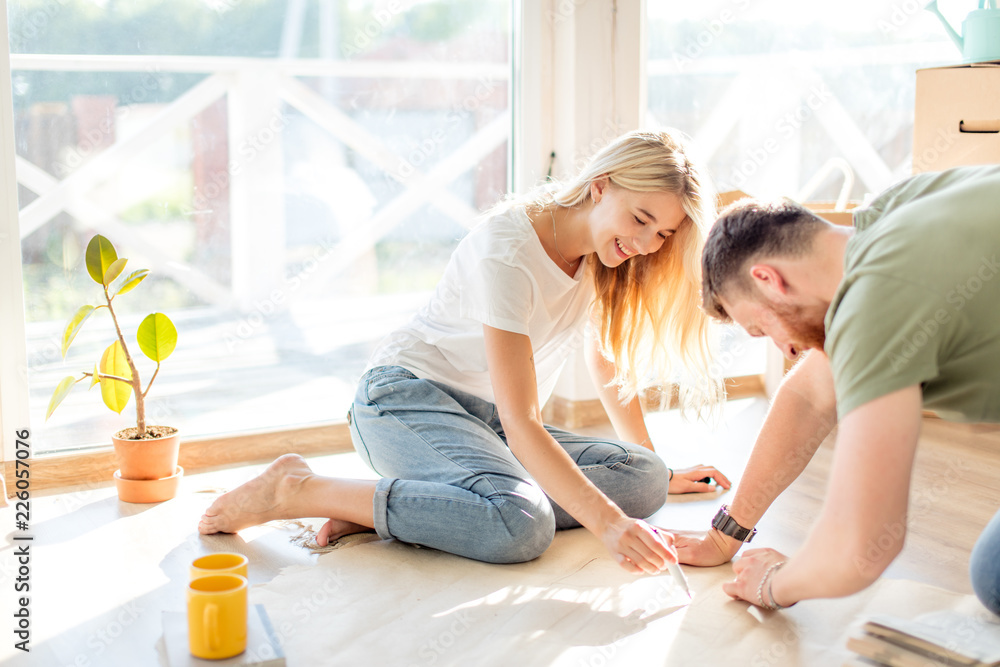 Young couple sitting at floor moving into new home looking at floor plans together
