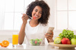 © Prostock-studio - Happy black woman texting on smartphone while eating salad