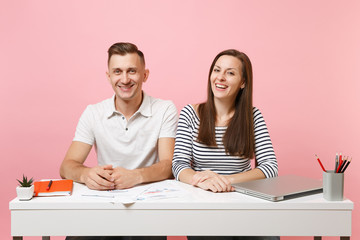 Two young smiling business woman man colleagues sit work at white desk with contemporary laptop isolated on pastel pink background. Achievement career concept. Copy space advertising, youth co working