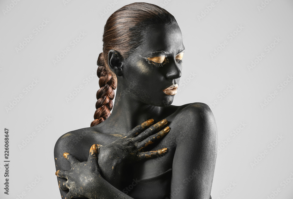 Beautiful woman with black and golden paint on her body against light background - obrazy, fototapety, plakaty 
