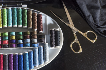 Sewing materials on the black background with metal scissors, close up