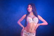 Woman in exotic costume sexually moves semi-nude body. Sexy traditional oriental belly dancer girl dancing on blue neon wall. Muslims, temptation concept. Spectacular show
