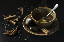 Close Up Of Brown Ceramic Cup With Hot Green Tea, Gingerbread Cookies, Dried Pears And Cinnamon On Dark Background