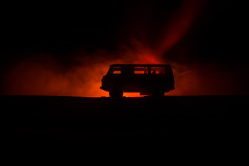 Wall Mural - Off roader jeep silhouette on dark toned foggy sky background. Car with light at night.