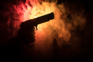 Male hand holding gun on black background with smoke ( yellow orange red white ) colored back lights