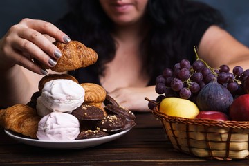Wall Mural - Sugar addiction, nutrition choices, conscious eating, overeating. Cropped portrait of overweight woman choosing between junk sweet food and fruits