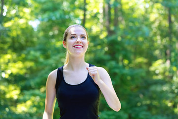 Wall Mural - Athletic young woman jogging on a bright summer day in the forest