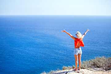 Wall Mural - Happy woman with hands up standing on cliff over sea. Travel mood, concepts of winner, freedom, happiness etc.